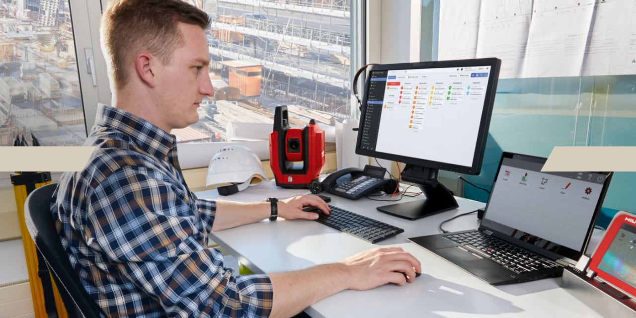 Mann sitzt im Büro vor seinem PC und arbeitet, auf einem Bildschirm hat er das Programm Fieldwire geöffnet. 