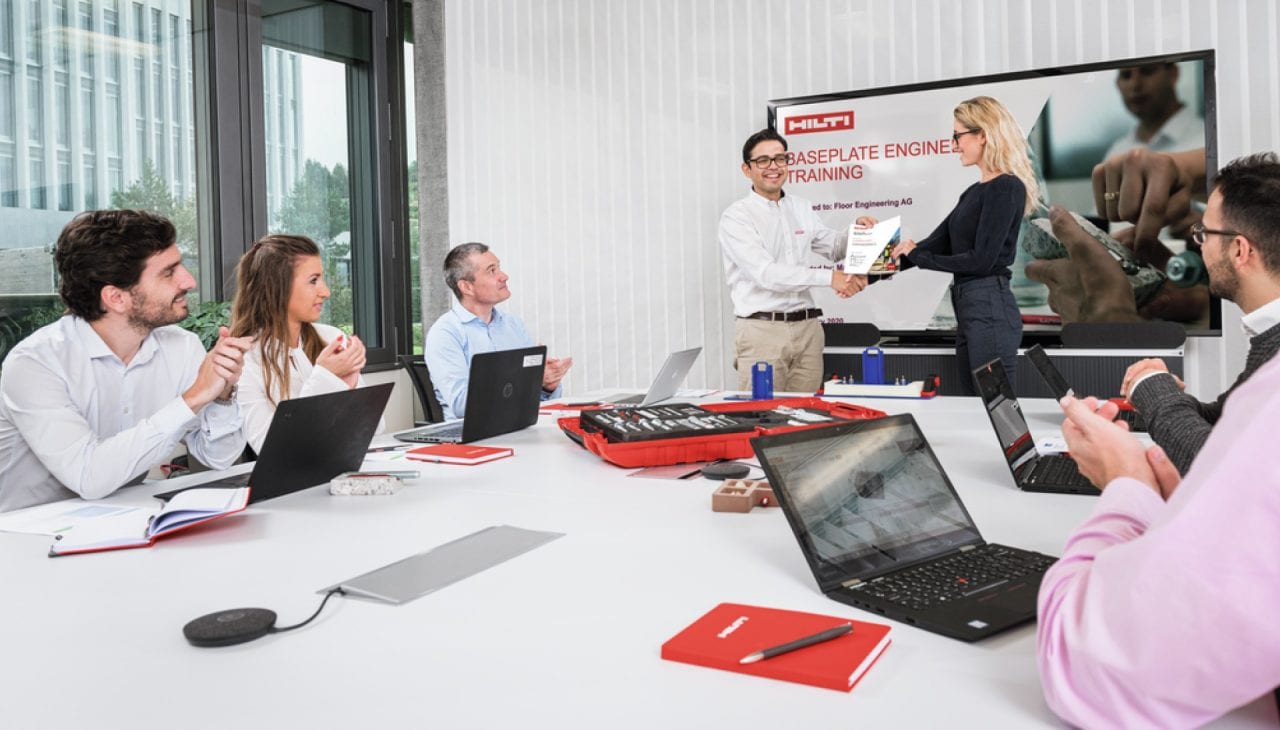 Eine Gruppe Männer und Frauen mit Laptops nimmt in einem Büroraum an einer Schulung teil.