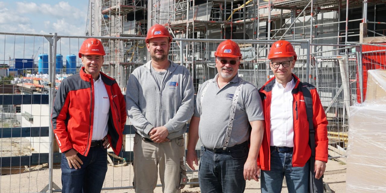 Vier Männer, einer davon mit einem Hilti Helm stehen lächelnd auf der Baustelle des “Roots”.