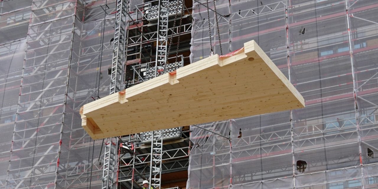 Ein Fertigbauteil aus Holz wird auf der Baustelle des “Roots” an Stahlseilen herabgelassen.