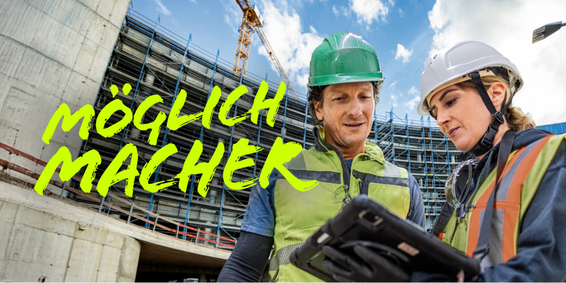 Ein Mann und eine Frau blicken gemeinsam vor einem Rohbau in ein Tablet.
