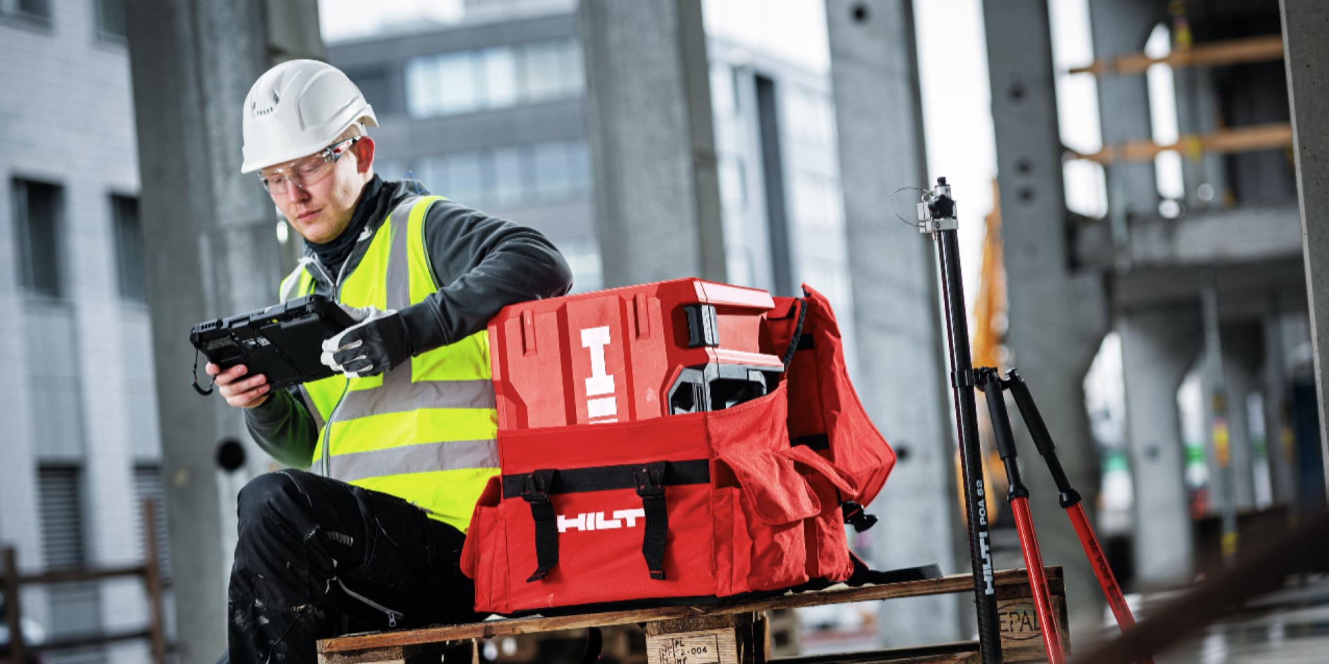 Eine Person in Arbeitskleidung vor Hilti Koffer schaut auf ein Tablet. 